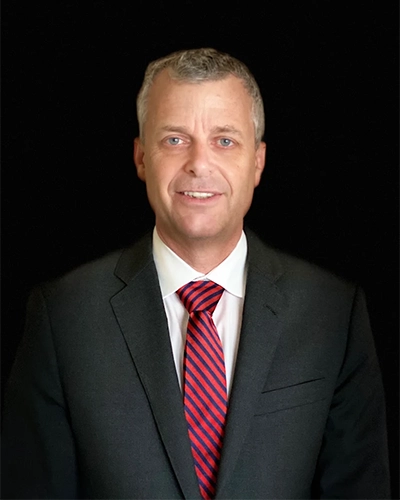 Eye Doctor Douglas Wike Smiling In A Suit In Front Of Black Background